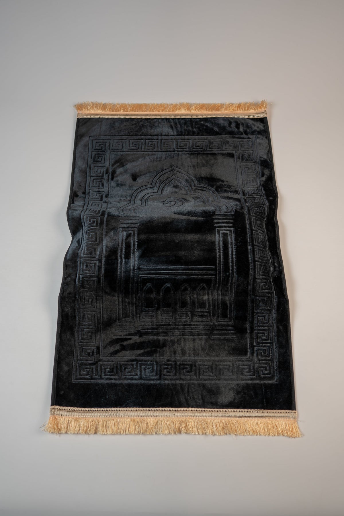 Ergonomic prayer mat in Black, top view with embossed mihrab design
