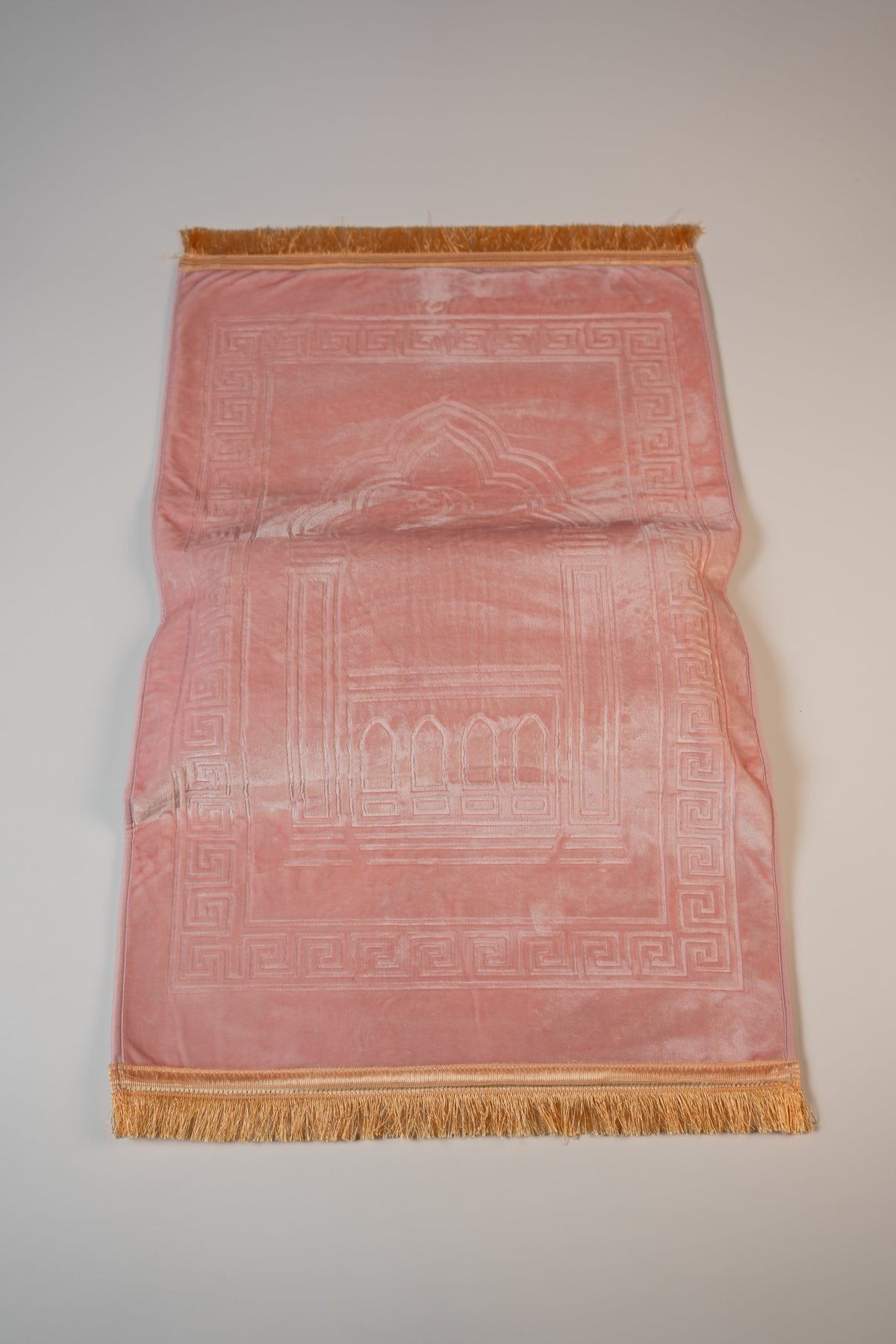 Ergonomic prayer mat in Pink, top view with embossed mihrab design